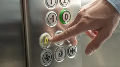 A hand presses the emergency button in the elevator.